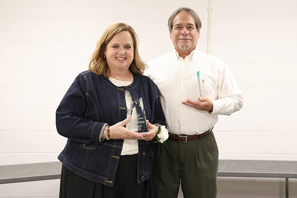 Two people stand with awards for years of service